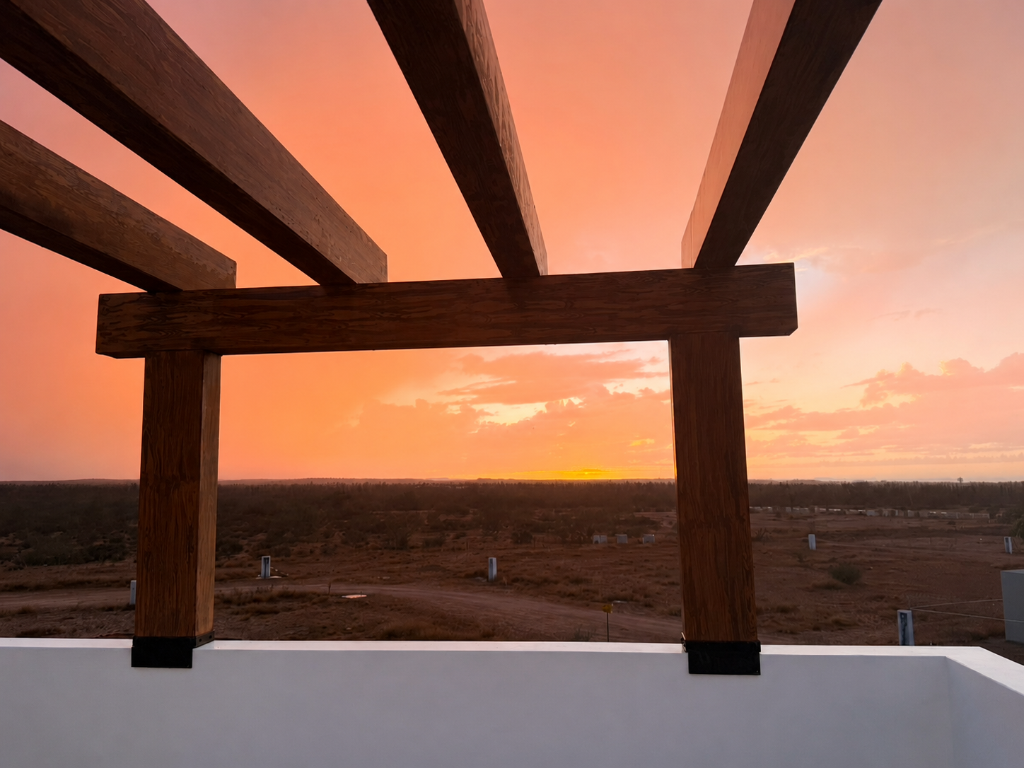 Rooftop pergola beams framing a coral desert sunset