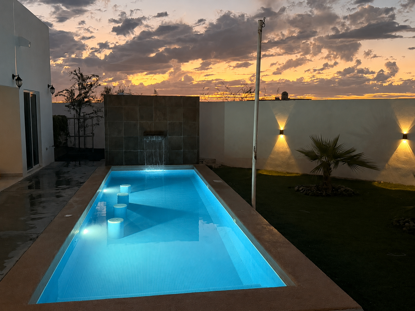 Courtyard pool at dusk with wall lights and a golden sky
